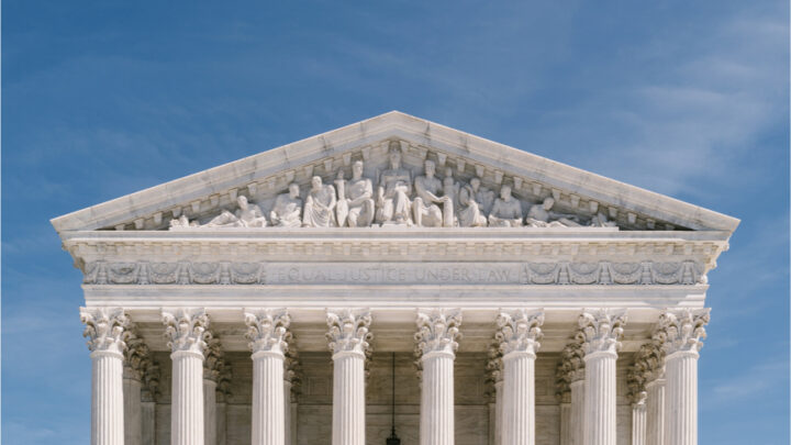 Front view of the U.S. Supreme Court building with its majestic columns supporting intricate sculptures on the facade, all under a clear blue sky.